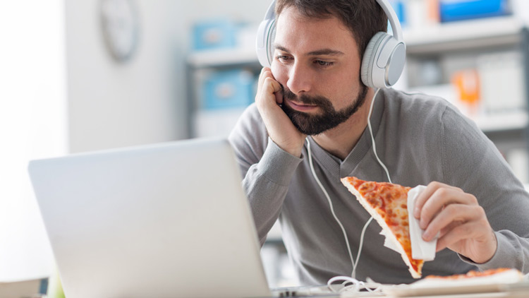 Mann isst neben Arbeit Pizza, Copyright Fotolia.com