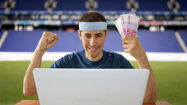 Person sitzt mit Laptop im Fußballstadion und freut sich über Gewinn, Copyright Panthermedia